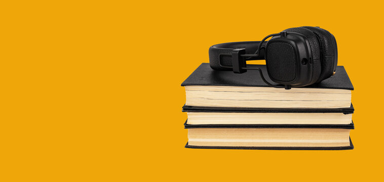 Banner with headphones on books stack on orange background. Listening to audiobooks concept. Audio storytelling. Education, literature study concept. Copy space