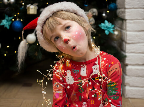 child in Christmas pajamas, Santa hat and a deer make-up painted on his face makes funny faces. Christmas, New Year, merry winter holidays, pampering at home. happy childhood. Cozy festive atmosphere