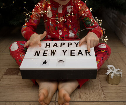 unrecognizable child in christmas pajamas holds a sign with congratulations Happy New Year. Cozy festive atmosphere. Waiting for the winter holidays, childhood