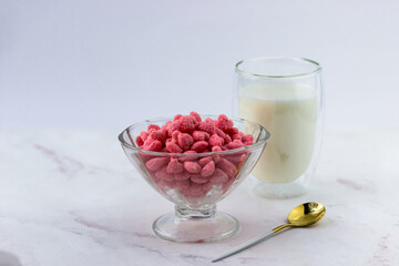 A bowl of breakfast cereal and a glass of milk on a white marble background. Snacks with raspberry flavor