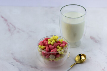 Snacks with raspberry and banana flavor in the shape of hearts and flowers. A bowl with a quick breakfast and a glass of milk on a white background
