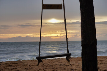 Close-up to a swing chair tied to a tree with a backdrop of the evening sea and the setting sun.