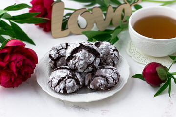 Treats on a white table. Chocolate cracks cookies, a cup of tea and peonies