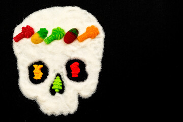 Unhealthy white sugar concept. Skull shape on a black background with a wreath of marmalade, candies, sweets. Concept about the dangers of sweets. Deceptive appearance of sweets as something useful
