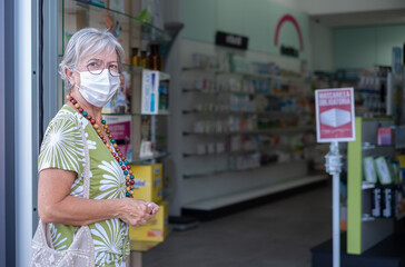 Senior woman wearing mask entering in pharmacy to buy medical products. Portrait of handsome elderly lady in drugstore pharmacy