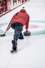 Curling game. Rear view of player playing curling on ice rink with granite stone and broom © svetlanais