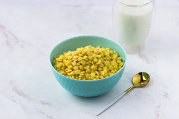 A bowl of breakfast cereal and a glass of milk on a white marble table. Instant corn flakes