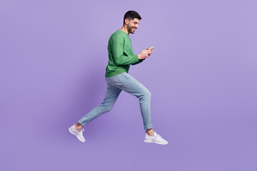 Fototapeta na wymiar Full length photo of young handsome hispanic man hold gadget jump read news dressed trendy green look isolated on violet color background