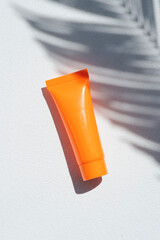 Plastic orange bottle for cream or lotion on a white background. Skincare cosmetic with beautiful palm shadows. Beauty concept for face body care