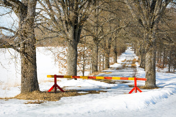 A red-yellow barrier preventing access to the forest. Covered in white snow on a bright sunny day.