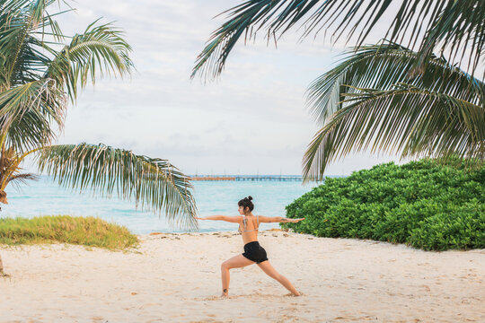 Woman doing yoga on the beach under the palm tree