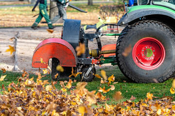 a tractor with a blower cleans a city park lawn and blows away autumn leaves, close-up