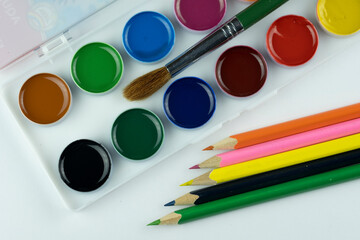Watercolor paints, a brush and colored pencils for children's creativity, isolated on a white background.