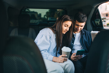 A young couple in the back seat of a taxi looks at their phone