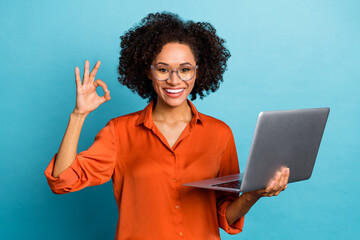 Portrait of beautiful trendy cheery wavy-haired girl using laptop showing ok-sign ad isolated on...