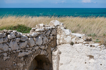 Ruiny kamiennych domów osady rybackiej w Gargano. Wybrzeże Adriatyku. W tle lazurowe morze i błękitne niebo. - obrazy, fototapety, plakaty