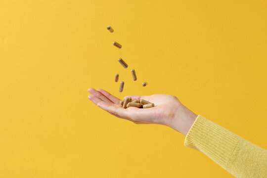 Flying pills, hands with drugs on yellow background