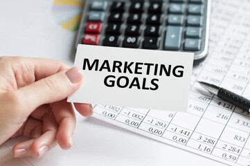 Marketing goals text on a card in the hands of a businessman in the background of an office desk