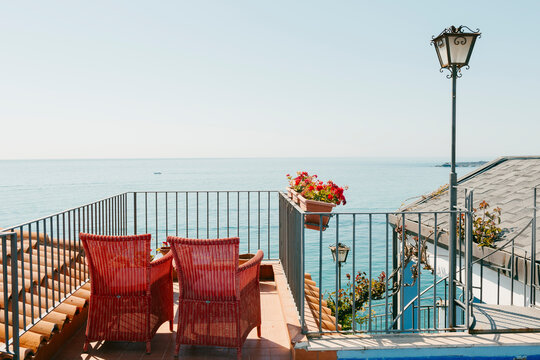 Small terrace with wicker red chairs facing view the Mediterranean sea