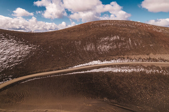 Monta&ntilde;a de color marr&oacute;n caf&eacute;, carretera de ripio y cielo azul con nubes