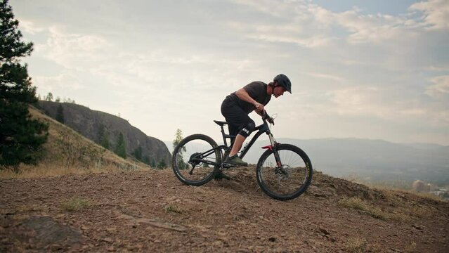 Wide of mountain biker getting on bike and riding in scenic mountain park