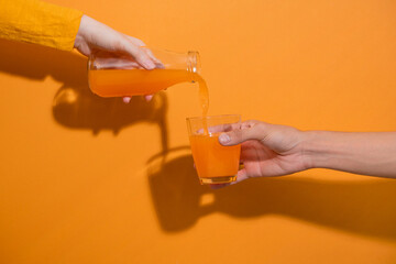Hand pouring orange juice from jug with ice into glass
