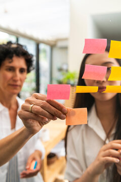 Multi-generational women freelancer putting post-it on glass board