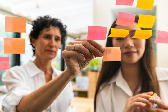 Multiracial businesswomen putting post-it notes on glass board