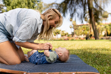 Mother Plays With Her Young Son On A Mat While Outdoors At the Park