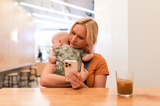 Concerned Mother Uses Cell Phone To Research While Holding Infant