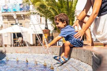 A child cooling off in the water fountain in the Plaza de España in Vejer de la Frontera, Cadiz. - obrazy, fototapety, plakaty