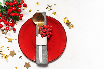 Festive Christmas table setting with red plate, napkin, cutlery set and festive decorations on white marble background top view.