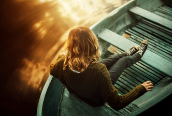 Top view of a blonde woman in a vintage green sweater and jeans sitting in an old fishing boat...