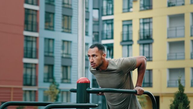 Professional gymnast strong sportsman push ups on parallel bars with straight body position pumping triceps trapezius arm muscles young athlete in sports uniform performing physical exercises outdoor