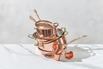 Stacked copper pans and cups on white marble surface.