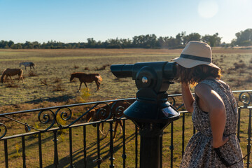A young tourist with binoculars looking at the horses grazing in the Doñana park, Santuario del...