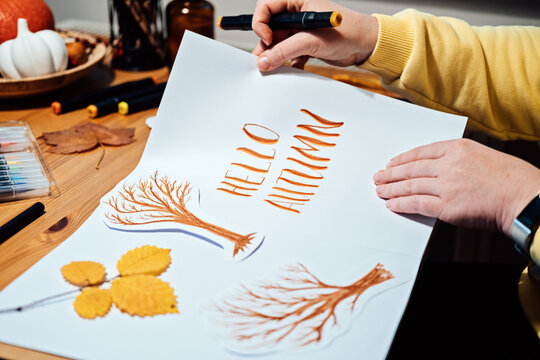 Autumn Season Drawing, How to draw fall lettering drawing and painting. Female hands drawing autumn lettering on the table with paints, brushes and autumn leaves