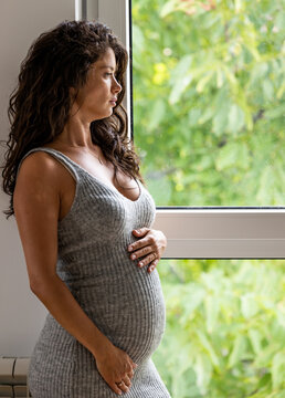 Pregnant woman holding hands on stomach beside windows
