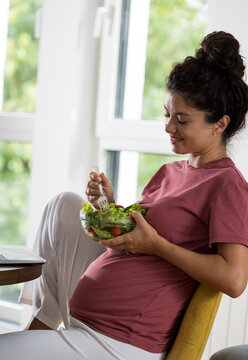 Pregnant woman eating salad in dining room