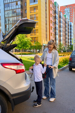 mother with a schoolboy child is standing near the car with a backpa