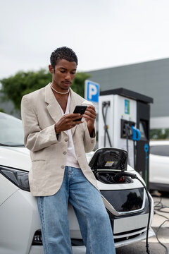 Black man having a coffee While Recharging Electric Vehicle