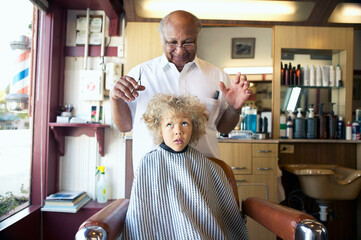 Barber getting ready to cut cute little boy's hair at barbershop