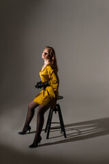 fashion model girl shooting in a mustard-colored dress on a white background on a cyclorama sitting on a chair subdued light 