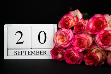 September 20 wooden calendar, white on a black background, pink roses lie nearby.Postcard with copy space. The concept of a holiday, congratulation, invitation, party, announcement, vacation,promotion
