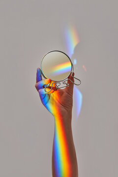 Hand holding round mirror with rainbow.