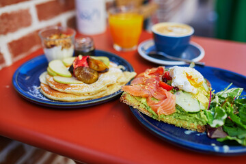 Delicious healthy brunch with avocado and salmon toast, boiled egg, pancakes with fruits and maple syrup