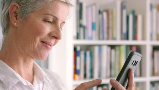 Mature woman, phone or thinking while reading internet news, funny blog or streaming comic movie in house library. Zoom on smile, happy or laughing senior with mobile research technology app in house