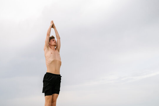 Man doing Mountain pose with arms up against cloudy sky