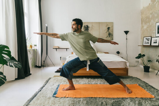Young Man Doing Warrior Pose in Bedroom