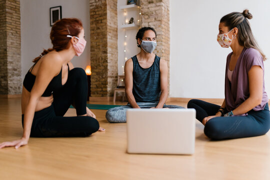 People in face masks near laptop in yoga studio